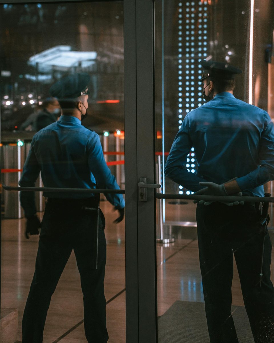 Security guards standing by glass doors at night.